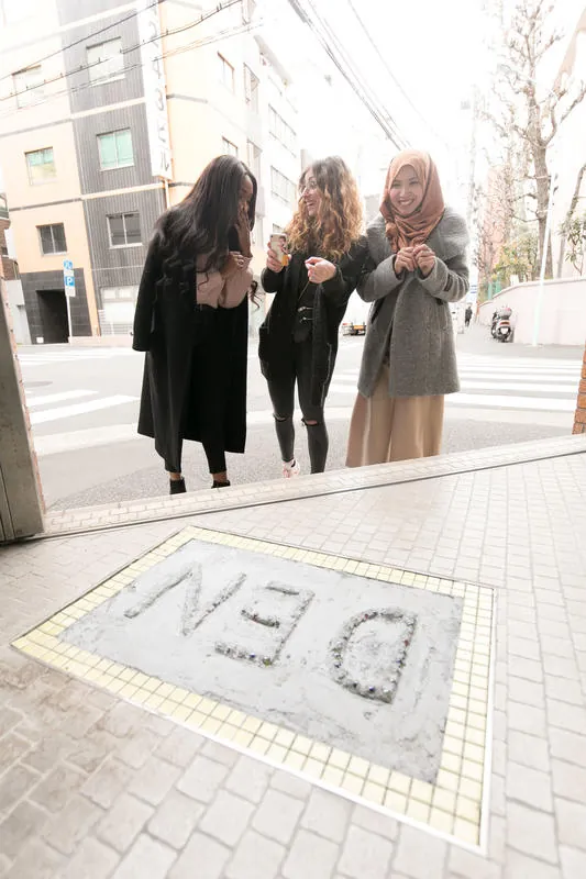 歩道に埋め込まれた「DEN」のモザイクと、そばを歩く3人