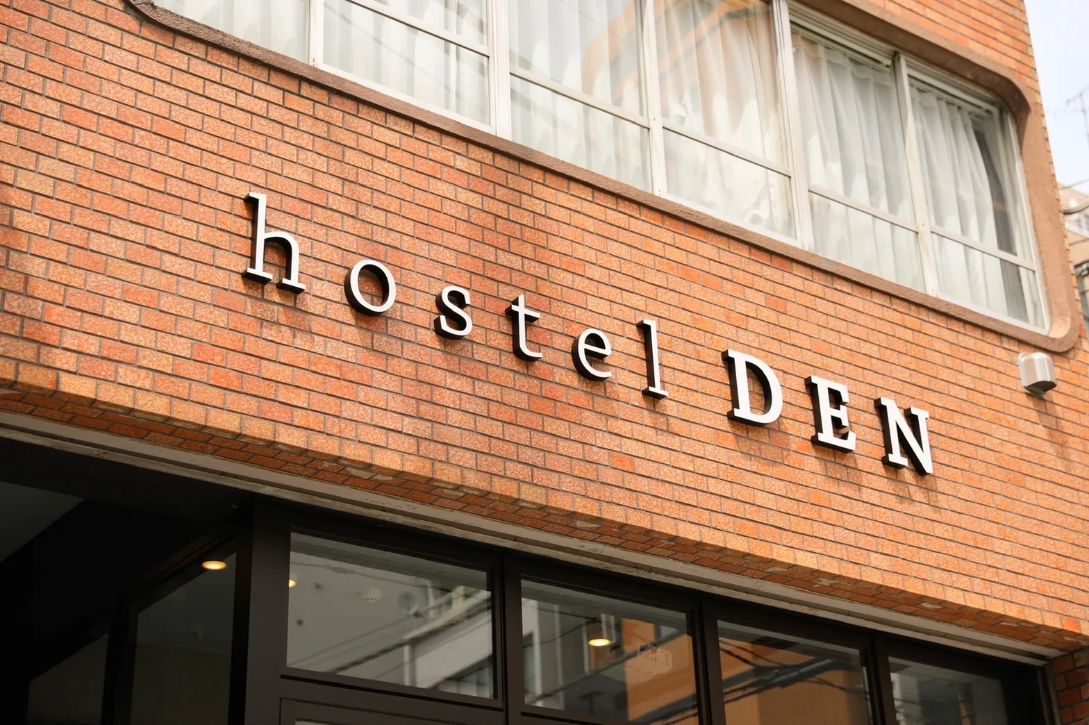 赤レンガの壁に掛かった銀色の「hostel DEN」の文字
